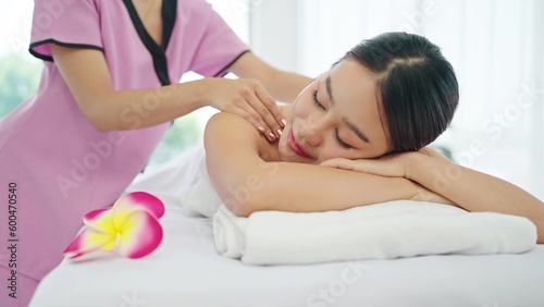 Happy and relaxed young Asian woman lying on massage bed closed eyes and relaxed while masseuse massaging back and shoulders. Body relaxation concept