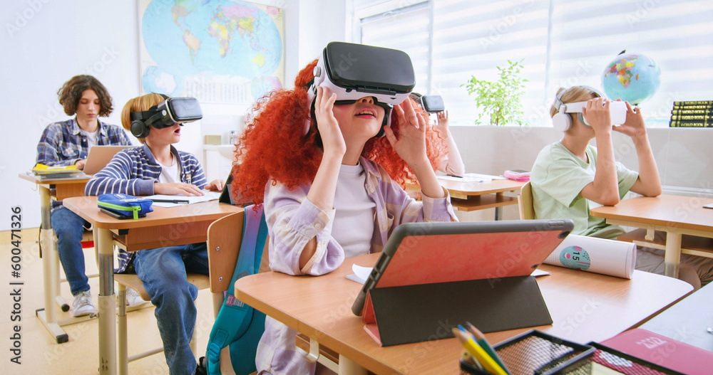 Interactive school concept. Kids in VR headsets sitting at desks and having virtual reality learning experience. Study technology. Kids in VR glasses in classroom. Tech education. - obrazy, fototapety, plakaty 