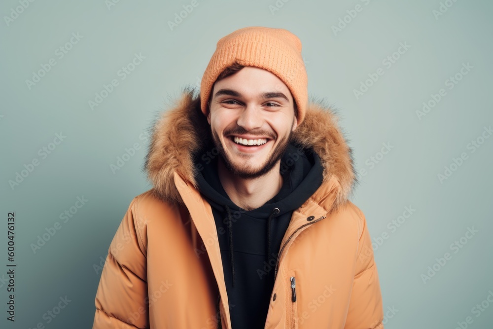 Portrait of a smiling young man in winter jacket and hat standing against blue background Portrait of a smiling young man in winter jacket and hat standing against blue background