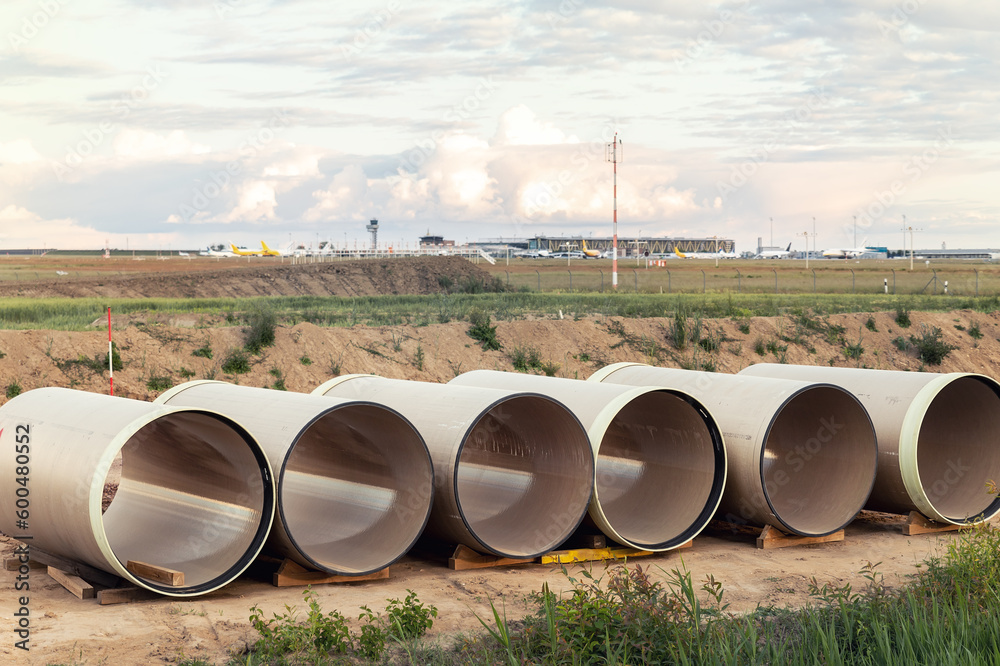 Stack of big frp composite fiberglass plastic sewage pipes at warehouse construction site near Leipzig Halle airport against blue sky background. Highway road construction infrastructure earthworks Stack of big frp composite fiberglass plastic sewage pipes at warehouse construction site near Leipzig Halle airport against blue sky background. Highway road construction infrastructure earthworks