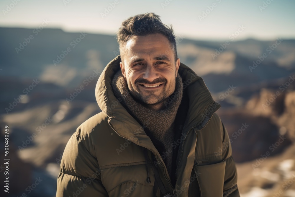 Handsome young man in warm jacket looking at camera and smiling while standing on the Grand Canyon Handsome young man in warm jacket looking at camera and smiling while standing on the Grand Canyon