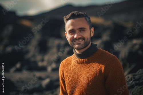 Portrait of a handsome young man in an orange sweater standing in the middle of the volcanic landscape
