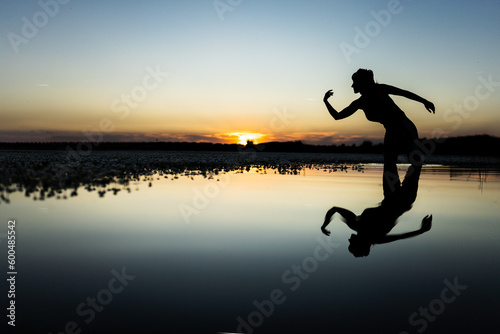 woman in the lake making figures and dancing with her body in the water  at sunset  with cold and warm colors in the sky  reflections in the water.
