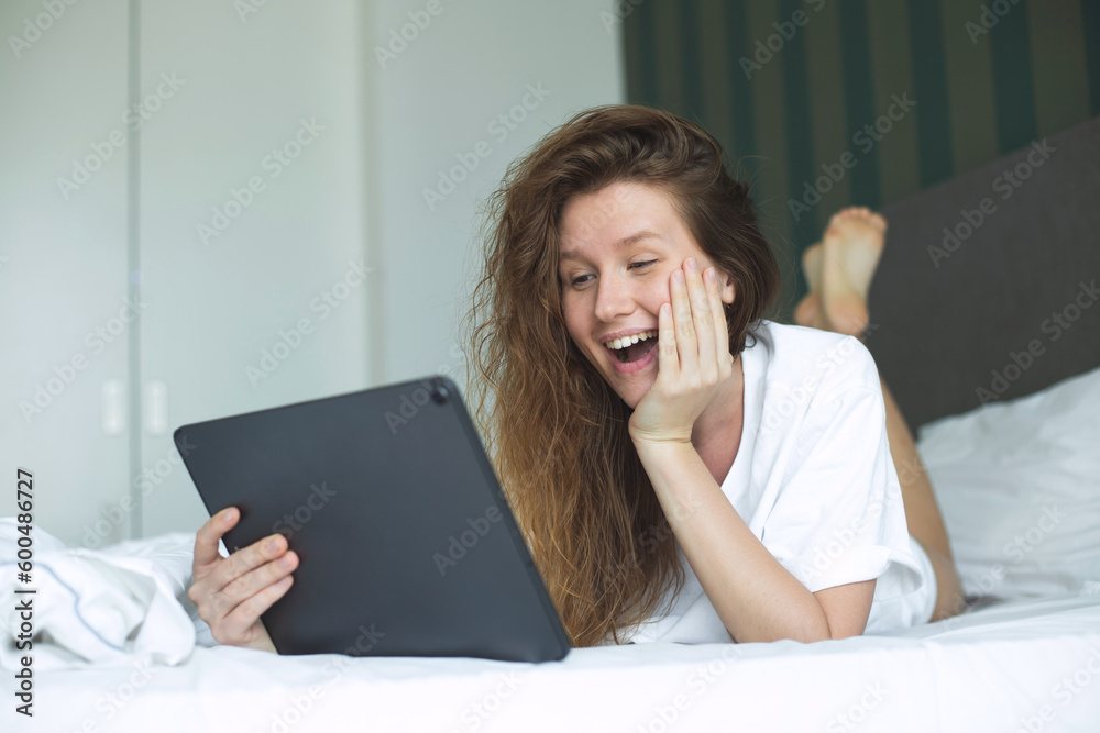 Happy young woman is using tablet computer at home in bed in bedroom, smile, have fun Happy young woman is using tablet computer at home in bed in bedroom, smile, have fun