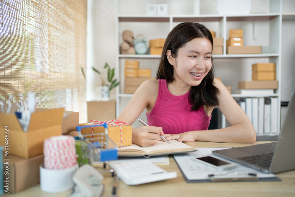 Woman is writing down the customer's details and addresses on the notebook or post box in order to prepare for shipping according to the information, Packing box, Sell online, Freelance working. Woman is writing down the customer's details and addresses on the notebook or post box in order to prepare for shipping according to the information, Packing box, Sell online, Freelance working.