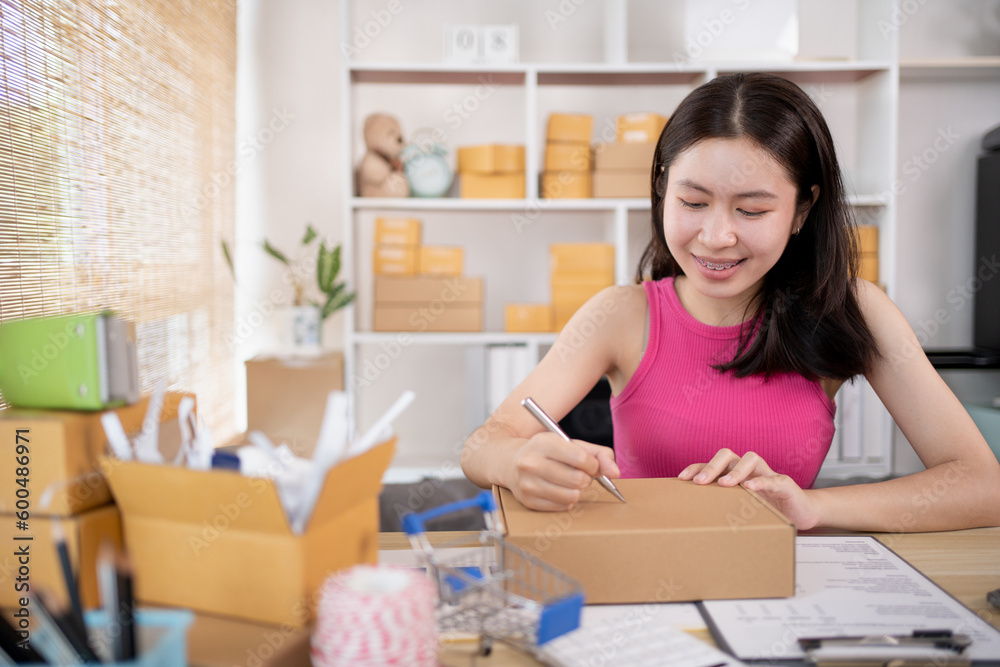 Woman is writing down the customer's details and addresses on the notebook or post box in order to prepare for shipping according to the information, Packing box, Sell online, Freelance working. Woman is writing down the customer's details and addresses on the notebook or post box in order to prepare for shipping according to the information, Packing box, Sell online, Freelance working.