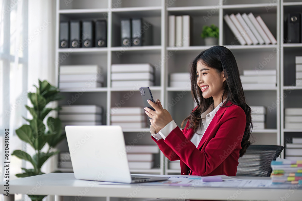 Young Asian businesswoman sit with her laptop computer happily talking on the phone with her customer explaining the detail in the office. Young Asian businesswoman sit with her laptop computer happily talking on the phone with her customer explaining the detail in the office.