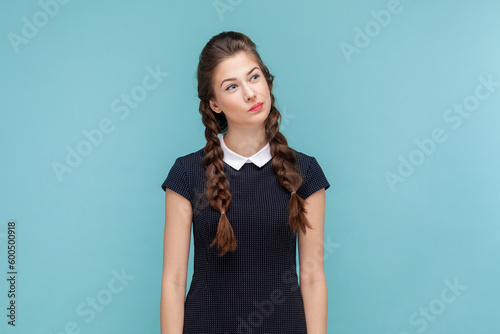 Portrait of pensive thoughtful woman with braids standing and looking away  making decision  thinks about solving problem  wearing black dress. woman Indoor studio shot isolated on blue background.