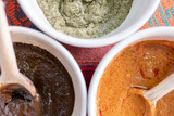 Three bowls with red, green and yellow mole sauce with a wooden spoon on top of a colorful traditional tablecloth