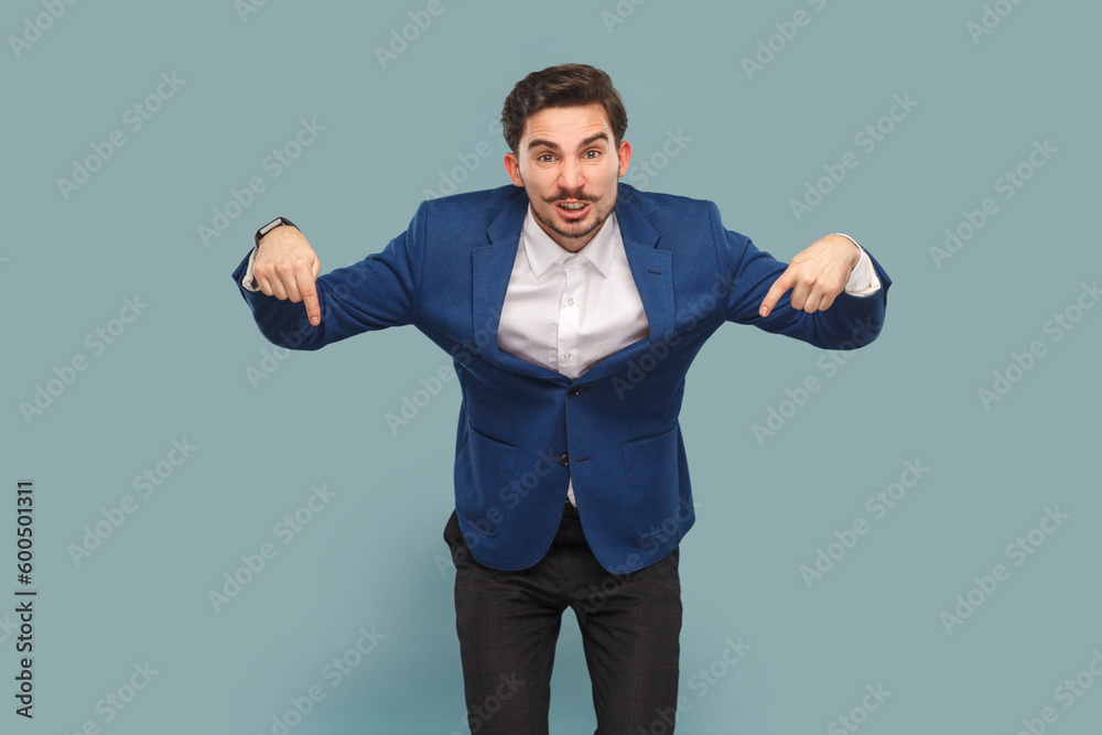 Angry man with mustache standing pointing down, giving command, looking at camera with serious expression, wearing white shirt and jacket. Indoor studio shot isolated on light blue background. Angry man with mustache standing pointing down, giving command, looking at camera with serious expression, wearing white shirt and jacket. Indoor studio shot isolated on light blue background.