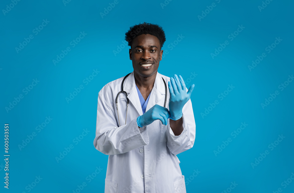 Smiling young african doc wearing medical gloves, blue background