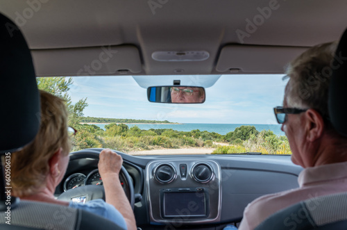 View of a blurred senior woman driving a car with her husband in copilot seat on a dirt road through wild Mediterranean coast.