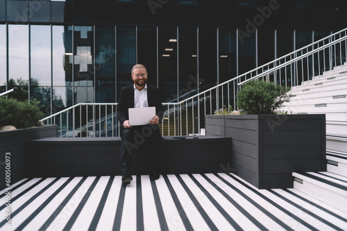 Happy businessman with laptop on street