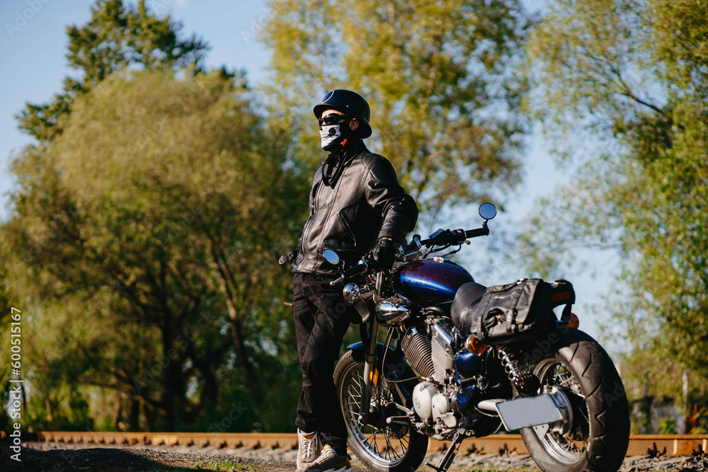 stylish male motorcyclist biker in mask and helmet with custom handmade motorcycle cruiser chopper. Stylish retro motorcycle stylish male motorcyclist biker in mask and helmet with custom handmade motorcycle cruiser chopper. Stylish retro motorcycle