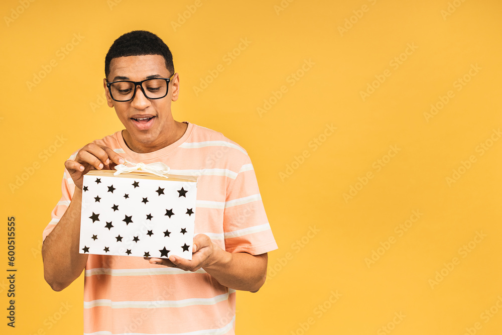 Cheerful smiling african american man holding wrapped present box. Happy young man congratulating, giving birthday gift, isolated on yellow background. - obrazy, fototapety, plakaty 