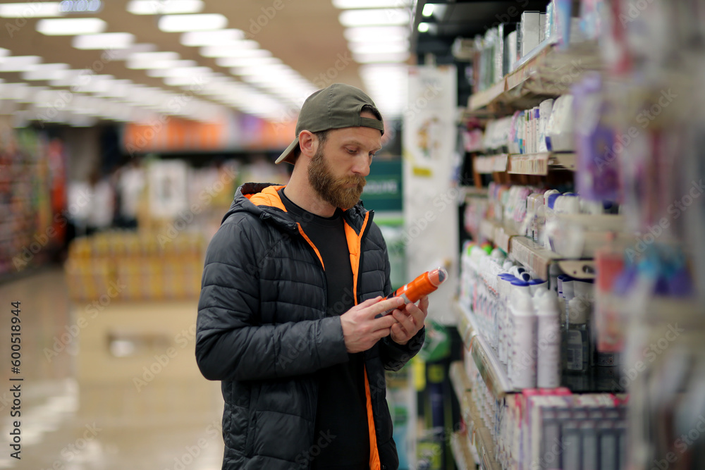 A bearded caucasian man customer is interested in a deodorant spray bottle at the grocery store, supermarket. Copy space for text, advertising, message, logo