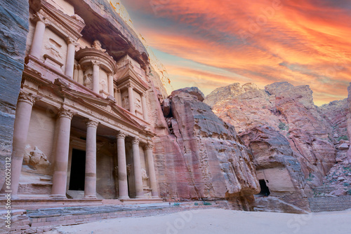 Front of Al-Khazneh (Treasury temple carved in stone wall - main attraction) in Lost city of Petra, orange sunset sky above