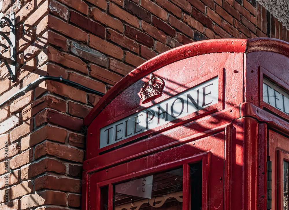 BURLINGTON, ONTARIO, CANADA-APRIL 7, 2023: Top of a British Red Phone Box is seen against a corner of a vintage brick wall with shadows of wires crossing the face. BURLINGTON, ONTARIO, CANADA-APRIL 7, 2023: Top of a British Red Phone Box is seen against a corner of a vintage brick wall with shadows of wires crossing the face.