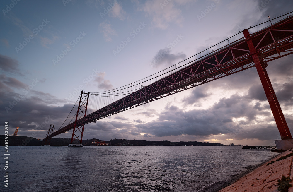 Beautiful landscape with suspension 25 April bridge over the Tagus river in Lisbon at night time, Portugal.