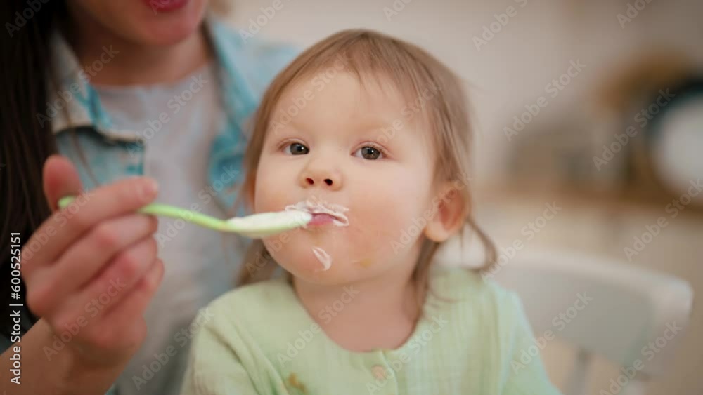 Mom feeding her baby with milk porridge at home. Portrait of baby toddler sitting in mother's hands. Raising child, motherhood, parenthood love and care in family, child's nutrition food concept. Mom feeding her baby with milk porridge at home. Portrait of baby toddler sitting in mother's hands. Raising child, motherhood, parenthood love and care in family, child's nutrition food concept.
