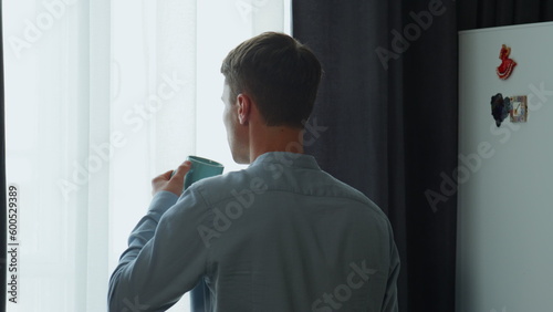 Back man drinking coffee looking window at morning. Guy thinking about success.