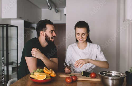 Carefree spouse enjoying bonding time on weekend cooking dinner togetherness and smiling at home kitchen, happy male and female 20s communicating while preparing salad of tomato and cucumber