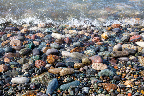 Multi-colored large pebbles on the beach, washed by a sea wave, glisten in the sun