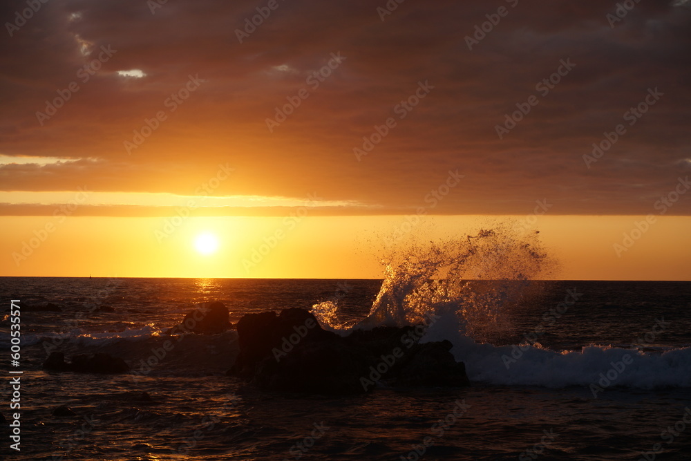 sunset over the sea with a wave crashing on a rock  on the tropical island of La Réunion, France