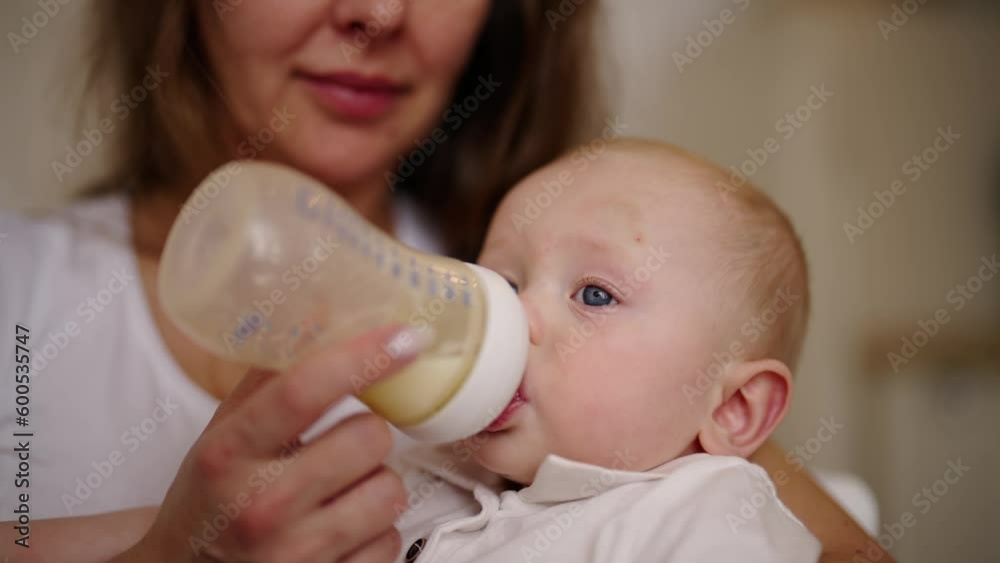 Mom feeding baby using bottle with milk mix kissing son to head. Mother holding child on hands during eating. Little boy eats from bottle. Babycare, maternity leave, babyhood motherhood concept. Mom feeding baby using bottle with milk mix kissing son to head. Mother holding child on hands during eating. Little boy eats from bottle. Babycare, maternity leave, babyhood motherhood concept.