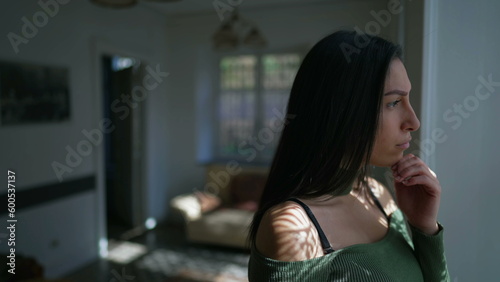 Photography One contemplative young woman standing by window looking outside with pensive expression