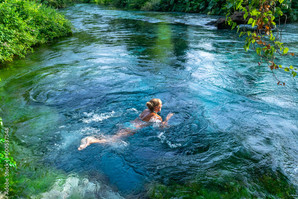 Tourist woman swiming into the unique karst source of water gushing from the ground called the Blue Eye or Syri i Kalter. Albania.