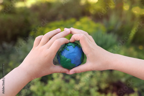 Fototapeta Naklejka Na Ścianę i Meble -  plasticine planet Earth in children's hands against the background of green plants. day earth, save environment concept