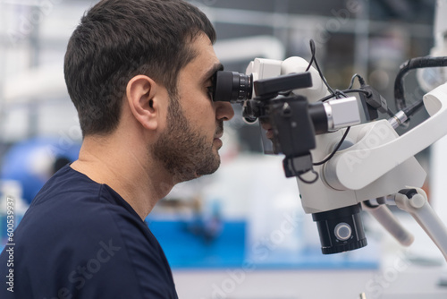 Focused doctor looking in innovative dental microscope to see teeth of patient in details professional medical equipment for cavity checkup bearded dentist in modern clinic