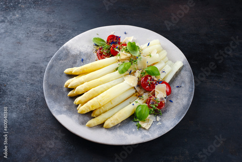 Weißer Spargel glasiert mit Kirschtomaten und Parmesan Käse serviert als close-up auf einem Design Teller mit Textfreiraum