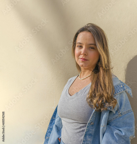 waist-up shot of a beautiful caucasian latin woman standing ahead a yellow wall on the street while looking at camera with a suptil smile