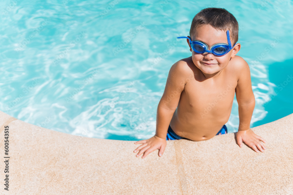Child on the edge of a pool looking at the camera with diving goggles