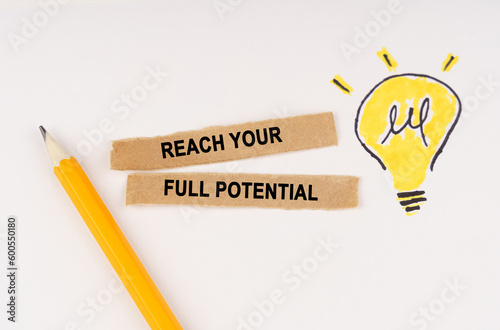 On a white surface, a luminous light bulb and pieces of paper with the inscription - REACH YOUR FULL POTENTIAL