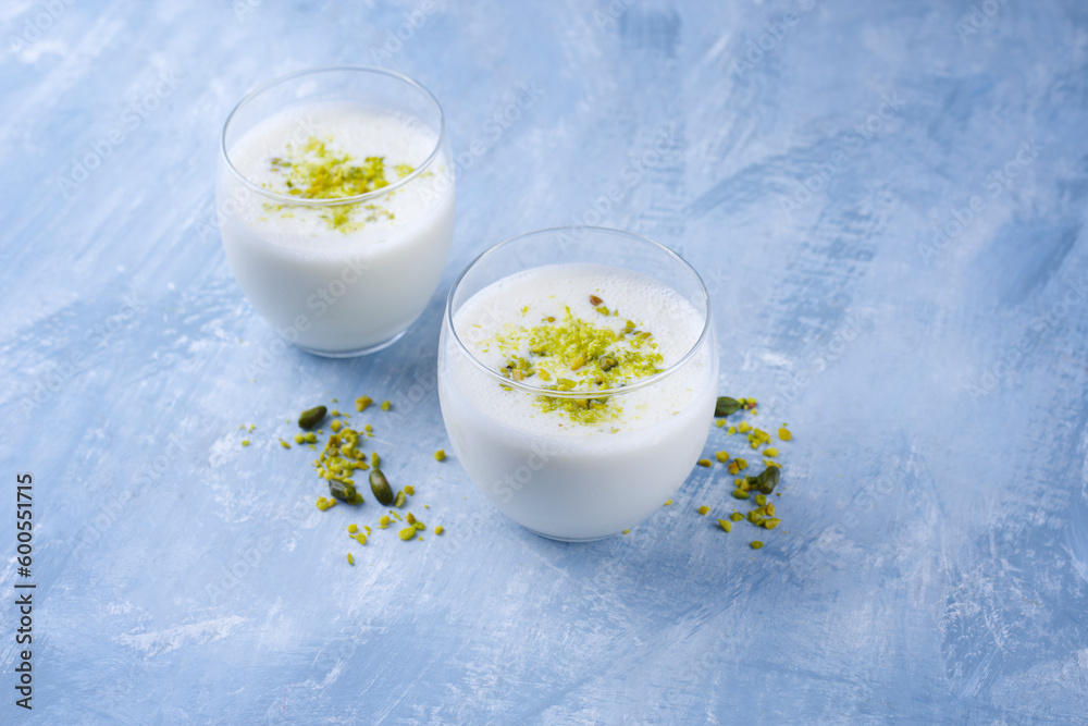 Traditional Indian lime lassi drink with dahi yogurt, lime and chopped pistachios served as close-up in a classical glass on a design plate with copy space Traditional Indian lime lassi drink with dahi yogurt, lime and chopped pistachios served as close-up in a classical glass on a design plate with copy space