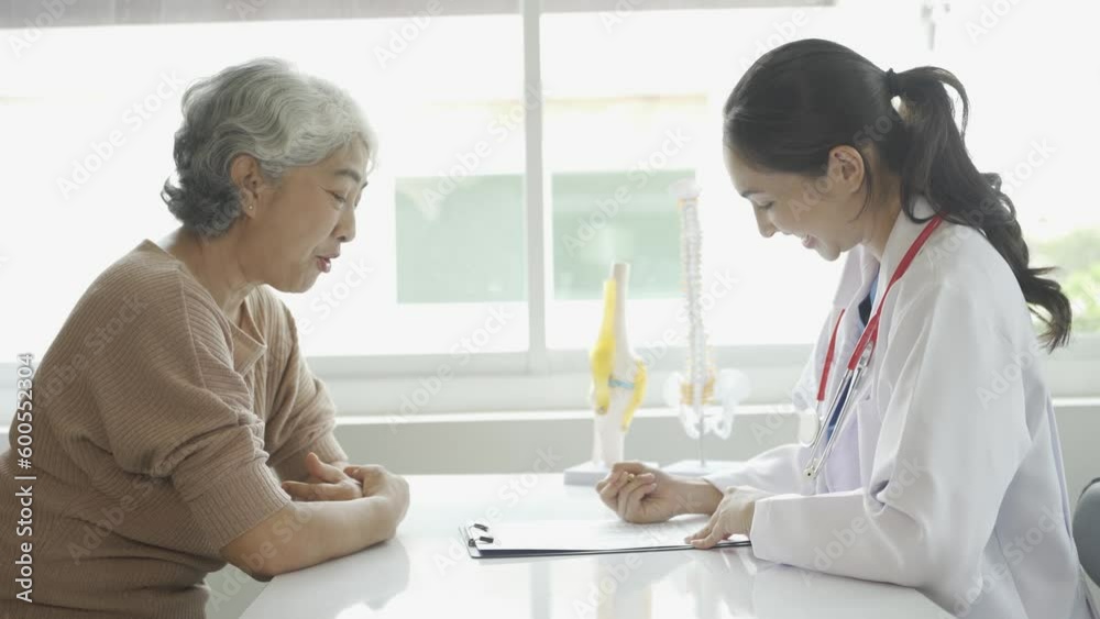 Female doctor consulting elderly patient and giving prescription sitting at table in clinic Osteoarthritis specialist, female doctor, looks at elderly people's medical history and talks, gives advice Female doctor consulting elderly patient and giving prescription sitting at table in clinic Osteoarthritis specialist, female doctor, looks at elderly people's medical history and talks, gives advice