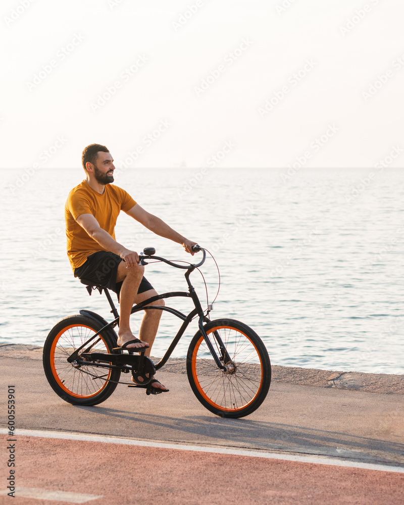 Carefree man with bicycle riding at sunset having fun and smiling