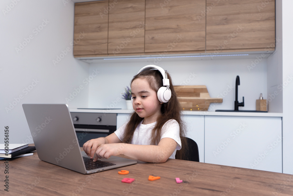 Elementary school student with wireless headphones talking to teacher online using laptop. Elementary school student with wireless headphones talking to teacher online using laptop.