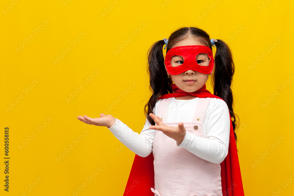 little asian girl in superman costume and mask shows with her hands to the side and advertises copy space little asian girl in superman costume and mask shows with her hands to the side and advertises copy space