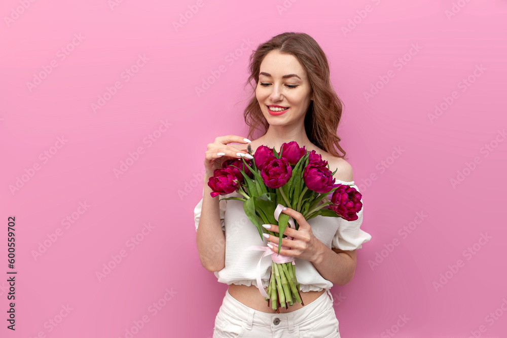 cute young woman in festive outfit holds bouquet of pink tulips and smells them on pink isolated background cute young woman in festive outfit holds bouquet of pink tulips and smells them on pink isolated background