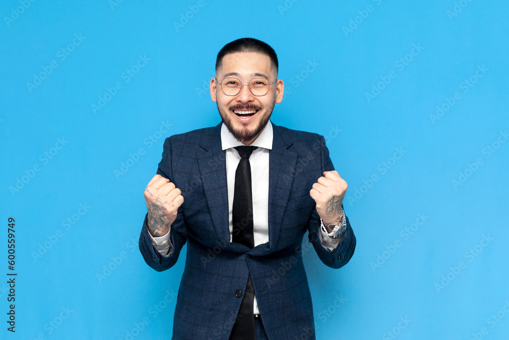 successful businessman asian winner in suit and glasses rejoice and celebrate victory on blue isolated background successful businessman asian winner in suit and glasses rejoice and celebrate victory on blue isolated background