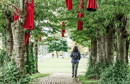 Burlington, Ontario, Canada - October 8, 2020: A young woman with a backpack walks a path underneath trees through the Red Dress Project installation for Missing and Murdered Indigenous Women