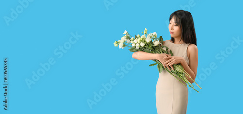Beautiful Asian woman holding bouquet of eustoma flowers on light blue background with space for text