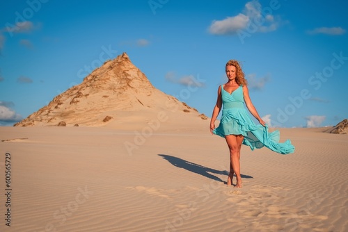 Beautiful blonde woman on hot sand with blue sky in the background. Photo taken on the shifting dunes over the Baltic Sea in Leba, Poland. Photo with a shallow depth of field with blurred background.