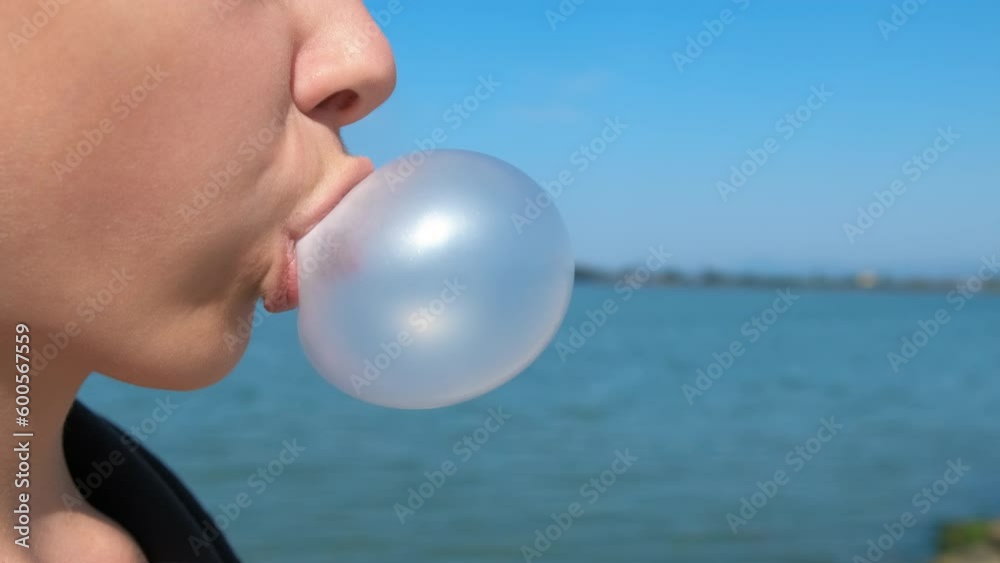 Teen make bubbles on the beach. A young tourist girl make a bubble from chewing gum on the sea shore in the day light.