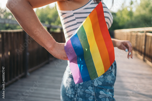 Close-up image of an unrecognizable young woman placing a rainbow flag banner in her pants pocket. LGTBIQ+ Concept