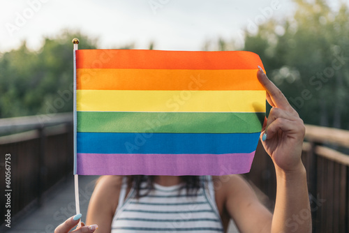 Unrecognizable young woman placing a rainbow flag horizontally in front of her face. LGTBIQ+ Concept